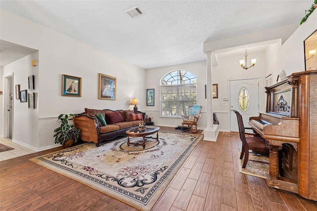 living room featuring decorative columns, an inviting chandelier, a textured ceiling, and hardwood / wood-style flooring