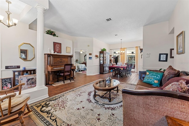 living room with decorative columns, hardwood / wood-style floors, ceiling fan with notable chandelier, and a textured ceiling