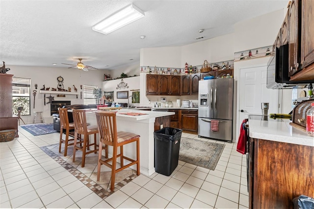 kitchen featuring ceiling fan, a kitchen breakfast bar, stainless steel fridge with ice dispenser, a textured ceiling, and light tile patterned flooring