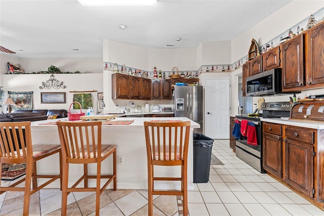 kitchen featuring a kitchen bar, a textured ceiling, stainless steel appliances, and kitchen peninsula