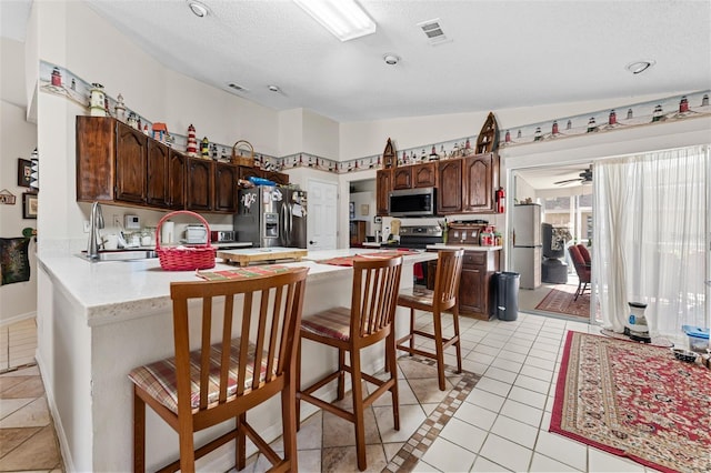 kitchen with a breakfast bar, kitchen peninsula, vaulted ceiling, dark brown cabinetry, and stainless steel appliances