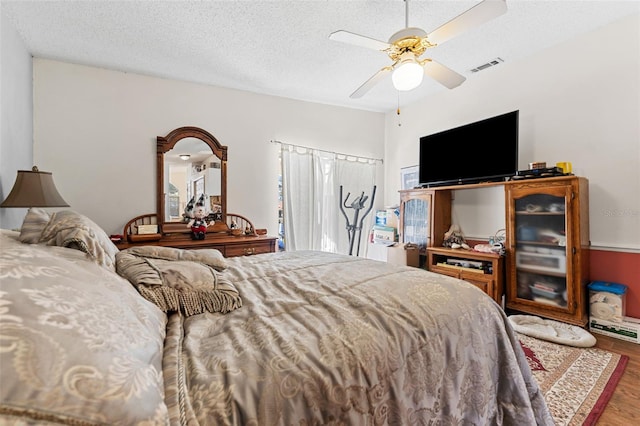 bedroom with ceiling fan, wood-type flooring, and a textured ceiling