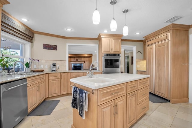 kitchen with light brown cabinetry, decorative light fixtures, sink, stainless steel appliances, and a center island with sink