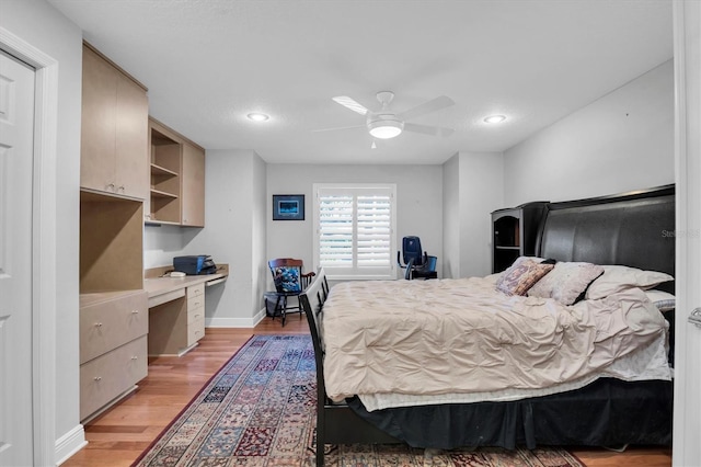 bedroom with built in desk, ceiling fan, and light hardwood / wood-style flooring