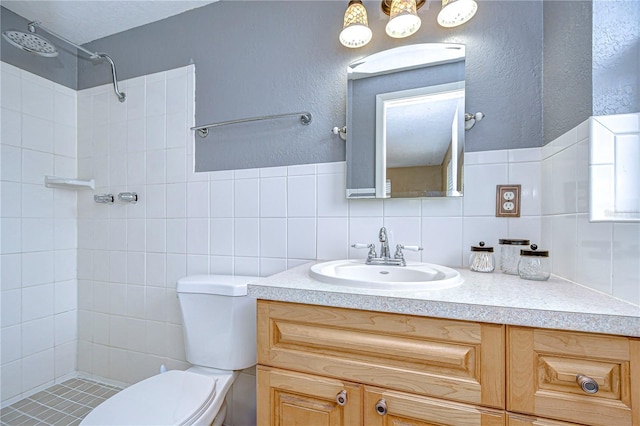 bathroom featuring vanity, toilet, tiled shower, tile walls, and tasteful backsplash