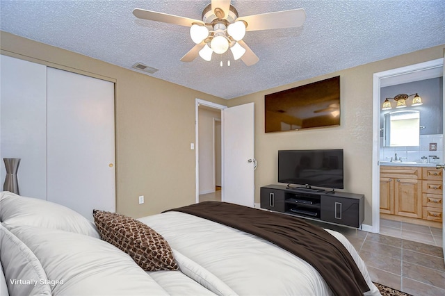 tiled bedroom with a textured ceiling, a closet, ensuite bath, and ceiling fan