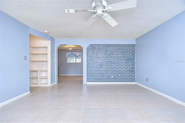 tiled empty room with built in shelves, ceiling fan, and a textured ceiling