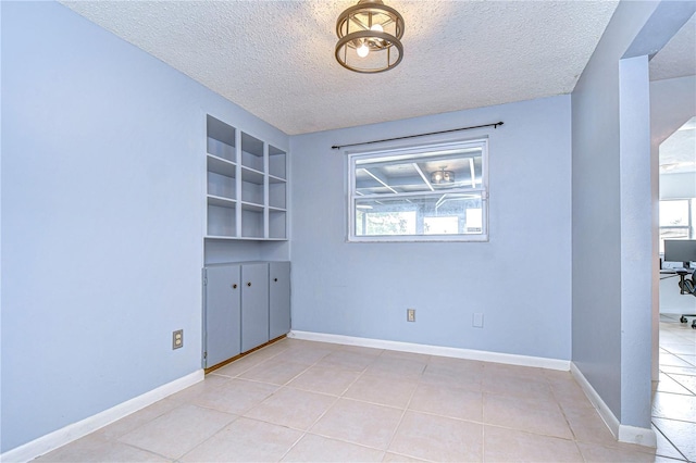 tiled empty room featuring built in shelves and a textured ceiling