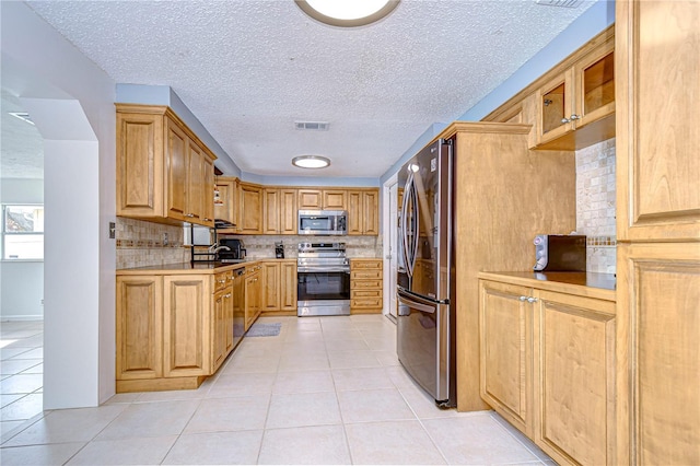 kitchen with tasteful backsplash, a textured ceiling, stainless steel appliances, sink, and light tile patterned floors