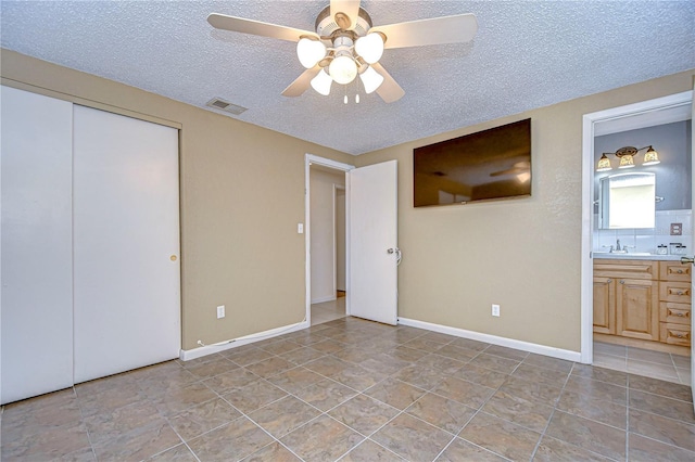 unfurnished bedroom with ensuite bath, ceiling fan, a closet, and a textured ceiling