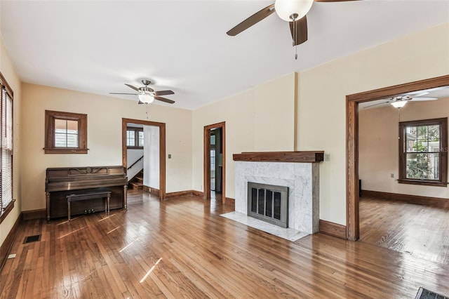 living room with baseboards, visible vents, ceiling fan, a premium fireplace, and wood finished floors