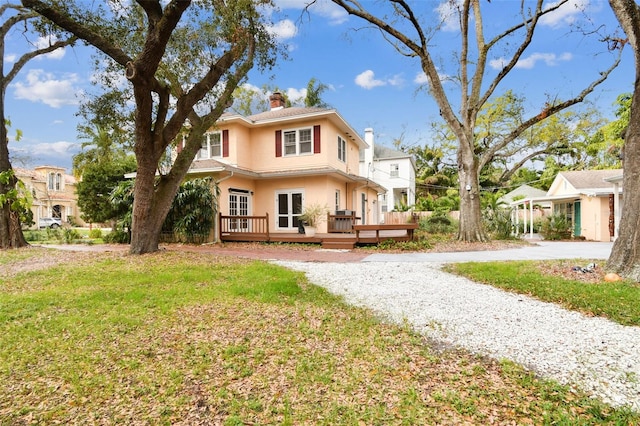 rear view of property with a lawn, a chimney, gravel driveway, a deck, and stucco siding