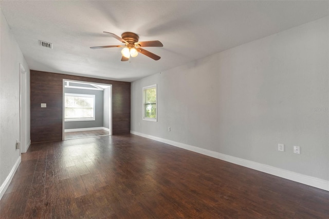 empty room with wooden walls, ceiling fan, and dark hardwood / wood-style floors