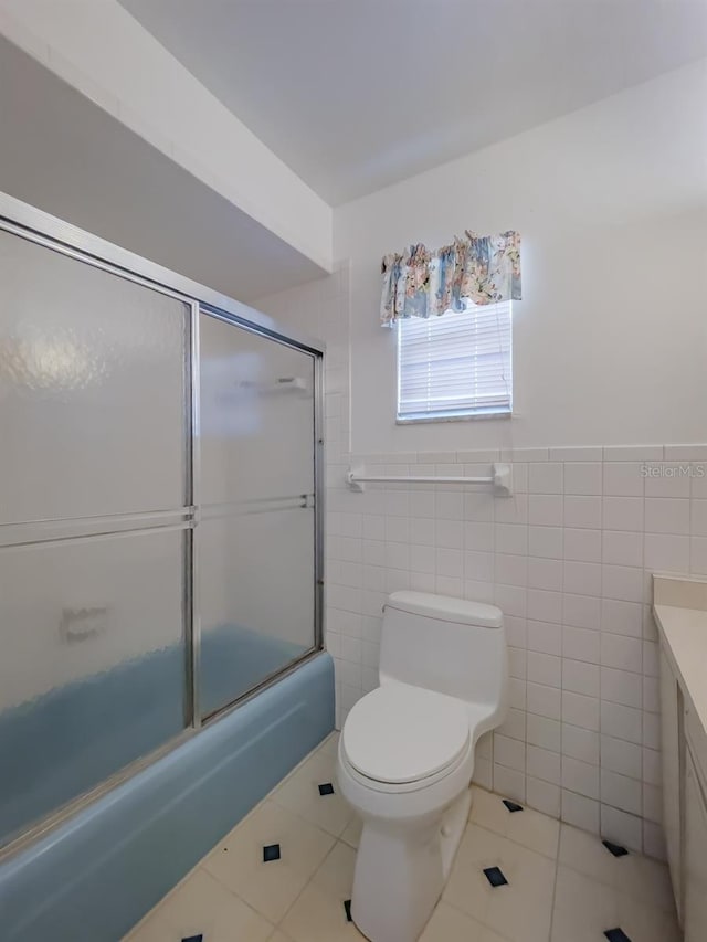 full bathroom with combined bath / shower with glass door, tile patterned floors, toilet, vanity, and tile walls