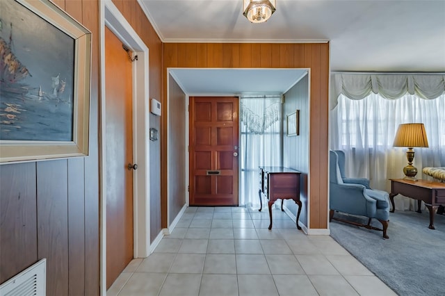 foyer entrance with wood walls, crown molding, and light carpet