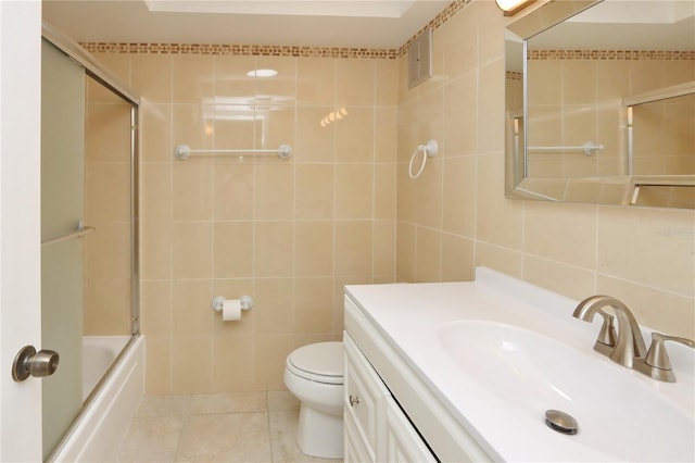 full bathroom with tile patterned flooring, toilet, shower / bath combination with glass door, vanity, and tile walls