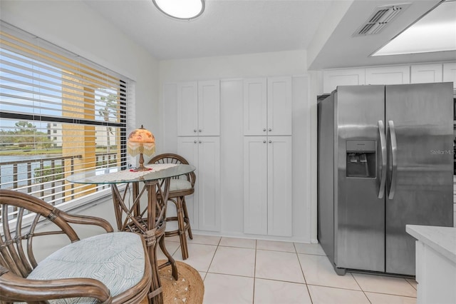 kitchen with light tile patterned floors, stainless steel refrigerator with ice dispenser, visible vents, and white cabinetry