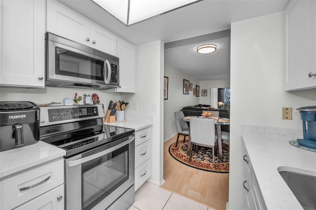 kitchen featuring white cabinets, light stone counters, open floor plan, stainless steel appliances, and a sink