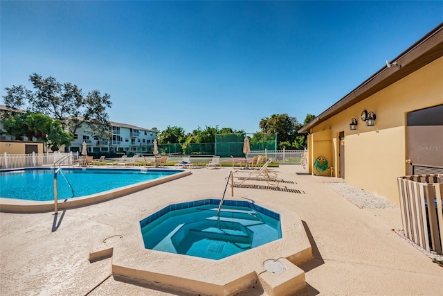 pool with a patio area, fence, and a hot tub