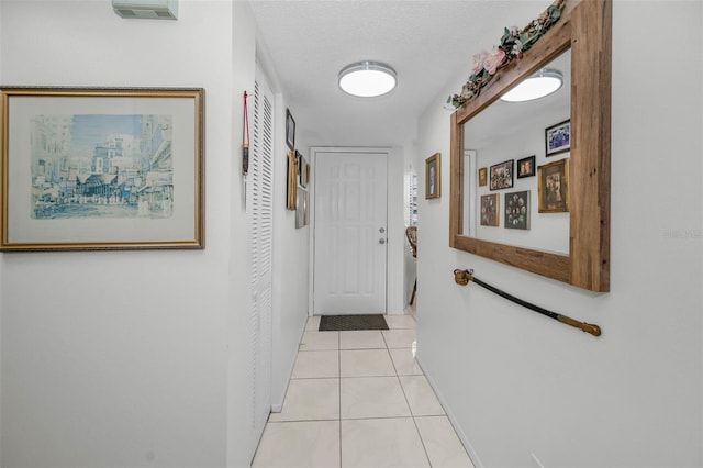 hallway featuring light tile patterned floors, baseboards, visible vents, and a textured ceiling