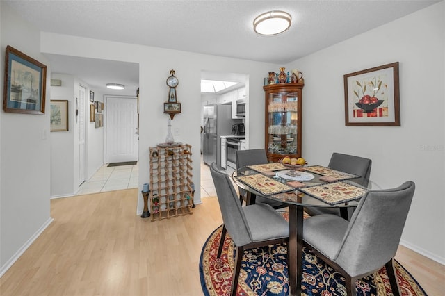 dining space with a textured ceiling, a skylight, baseboards, and light wood-style floors