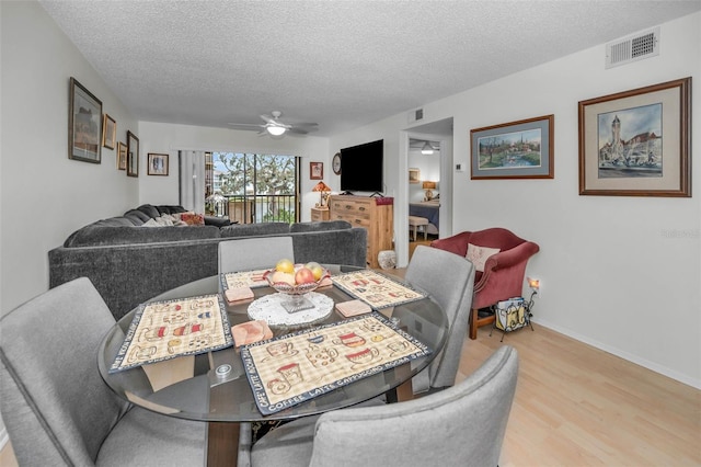 dining space with a ceiling fan, a textured ceiling, visible vents, and wood finished floors