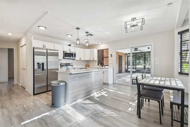 kitchen featuring stainless steel appliances, light hardwood / wood-style flooring, white cabinets, a center island, and hanging light fixtures