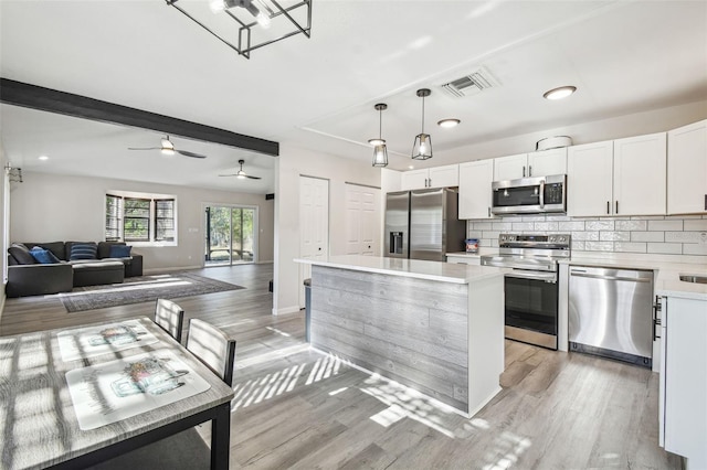 kitchen featuring light wood-type flooring, stainless steel appliances, a kitchen island, pendant lighting, and white cabinetry