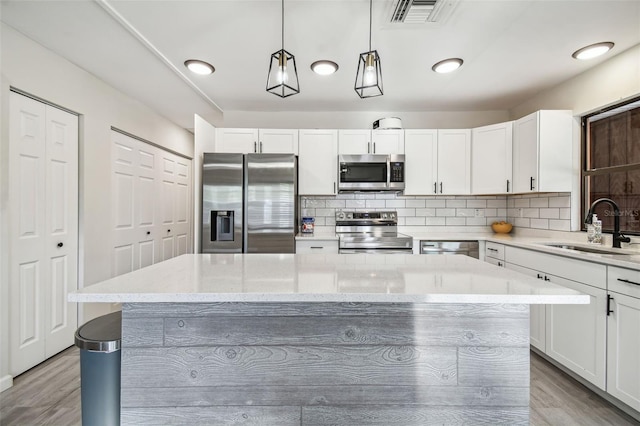 kitchen featuring white cabinets, sink, decorative light fixtures, light hardwood / wood-style floors, and stainless steel appliances