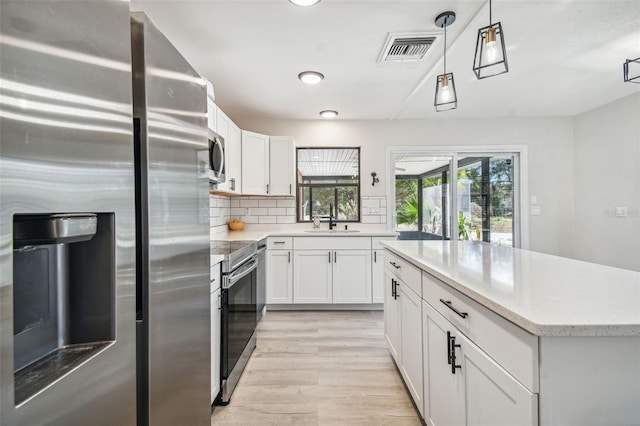 kitchen featuring sink, appliances with stainless steel finishes, decorative light fixtures, light hardwood / wood-style floors, and white cabinetry