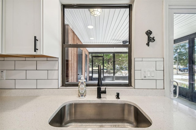 details featuring white cabinets, backsplash, light stone countertops, and sink