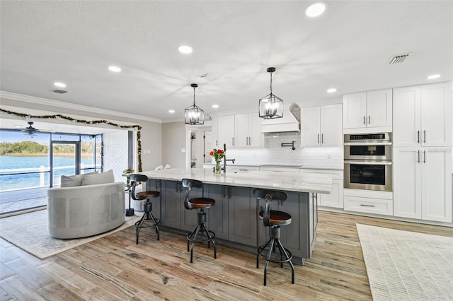 kitchen featuring hanging light fixtures, white cabinets, stainless steel double oven, and light hardwood / wood-style flooring