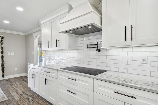 kitchen with black electric stovetop, custom range hood, crown molding, hardwood / wood-style floors, and white cabinetry