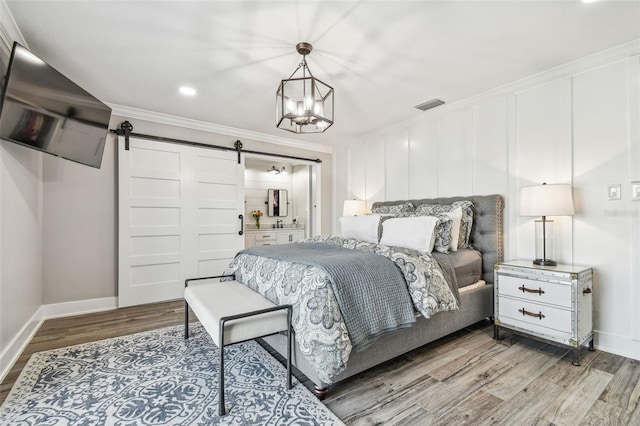 bedroom featuring connected bathroom, an inviting chandelier, a barn door, light hardwood / wood-style floors, and ornamental molding