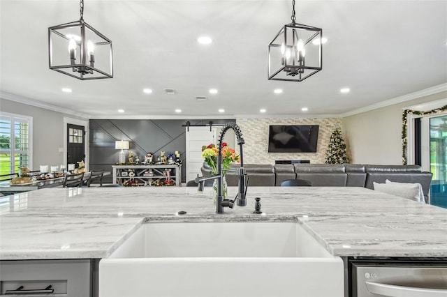 kitchen featuring sink, crown molding, a barn door, decorative light fixtures, and light stone counters