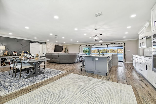 kitchen with a kitchen island with sink, white cabinets, a barn door, light hardwood / wood-style floors, and a kitchen bar