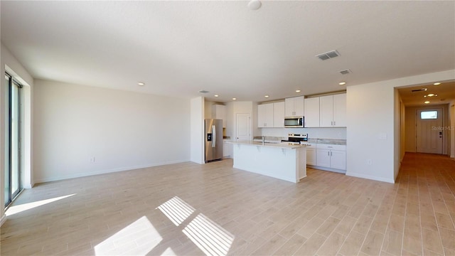 kitchen with white cabinets, an island with sink, light wood-type flooring, and appliances with stainless steel finishes