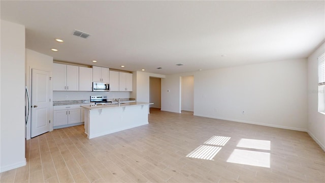 kitchen with light wood-type flooring, stainless steel appliances, white cabinetry, and a kitchen island with sink