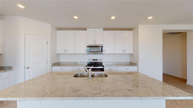 kitchen with a center island with sink, white cabinets, sink, light hardwood / wood-style flooring, and appliances with stainless steel finishes