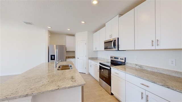 kitchen with white cabinets, sink, stainless steel appliances, and an island with sink