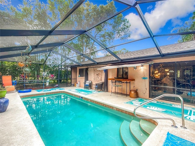 view of pool with exterior bar, glass enclosure, and a patio area