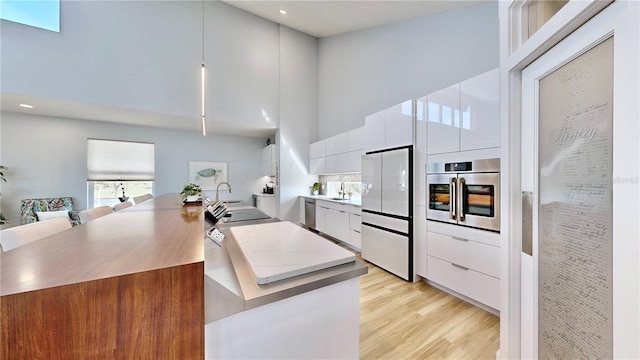 kitchen with a towering ceiling, modern cabinets, white cabinetry, and appliances with stainless steel finishes