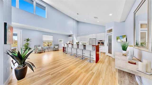 interior space featuring visible vents, baseboards, light wood-style floors, high vaulted ceiling, and recessed lighting