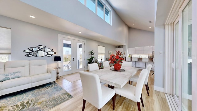 dining space with a towering ceiling, light wood-type flooring, a wealth of natural light, and french doors