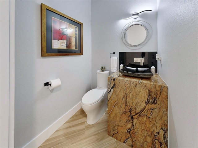 half bath with wood finished floors, toilet, and baseboards