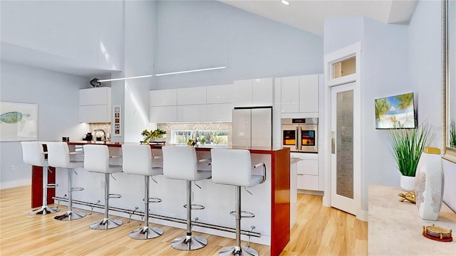 10101 Eagle Preserve Dr, Englewood, FL 34224 - kitchen with appliances with stainless steel finishes, high vaulted ceiling, light wood-style flooring, white cabinets, and a breakfast bar