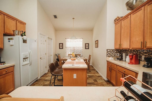 kitchen featuring white fridge with ice dispenser, decorative light fixtures, a breakfast bar area, decorative backsplash, and a kitchen island