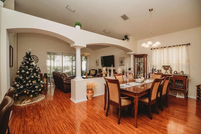 dining space featuring a notable chandelier, wood-type flooring, and decorative columns