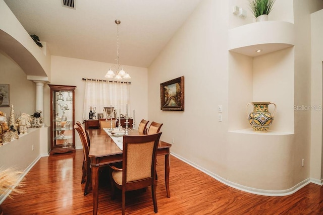 dining area featuring hardwood / wood-style flooring, vaulted ceiling, ornate columns, and an inviting chandelier