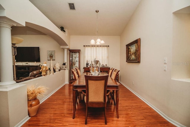 dining area with wood-type flooring, an inviting chandelier, and ornate columns